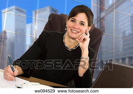 Stock Photo - Caucasian businesswoman setting in an office at a desk and smiling. Fotosearch