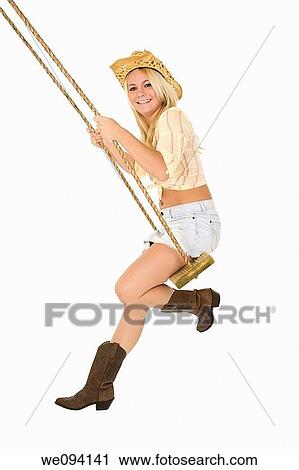 Stock Image - Caucasian cowgirl in wooden swing on white background. Fotosearch