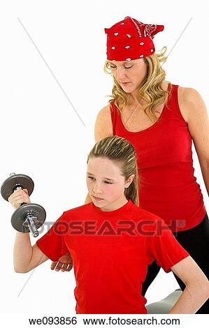 Stock Photograph - Caucasian mother helping her preteen daughter to lift weights using a dumbbell on a white background. Fotosearch