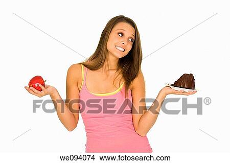 Caucasian woman holding an apple and slice of chocolate cake trying to decide which one to eat View Large Photo Image Picture - Caucasian woman holding an apple and slice of chocolate cake trying to decide which one to eat. Fotosearch
