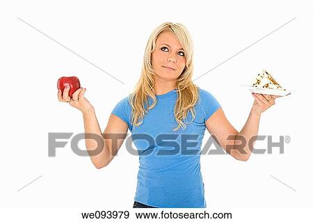 Caucasian woman holding an apple and slice of cake trying to decide which one to eat View Large Photo Image Stock Photo - Caucasian woman holding an apple and slice of cake trying to decide which one to eat. Fotosearch