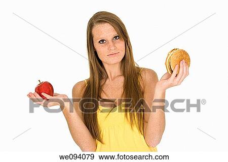 Caucasian woman holding an apple and hambuger trying to decide which one to eat View Large Photo Image Stock Photo - Caucasian woman holding an apple and hambuger trying to decide which one to eat. Fotosearch