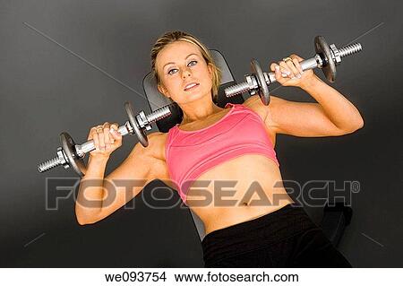 Caucasian woman in early 20s lifting weights using a dumbbell on a gray background View Large Photo Image Picture - Caucasian woman in early 20s lifting weights using a dumbbell on a gray background. Fotosearch