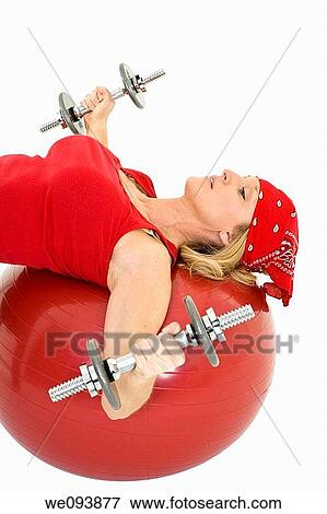 Stock Photo - Caucasian woman in early 40s lifting weights using a excerise ball and dumbbell on a white background. Fotosearch