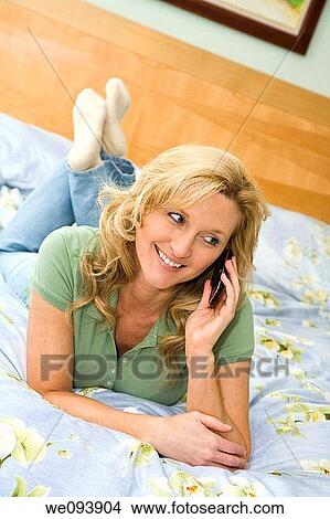 Caucasian woman in late 30s laying in bed talking on a cell phone View Large Photo Image Picture - Caucasian woman in late 30s laying in bed talking on a cell phone. Fotosearch