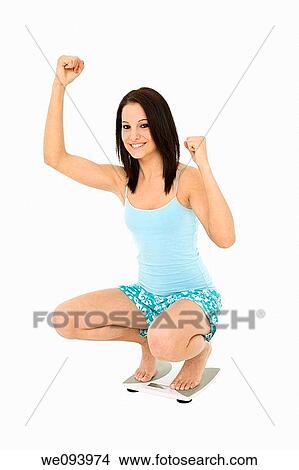 Picture - Caucasian woman standing on a scale weighting herself and very upset. Fotosearch