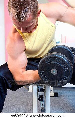 Stock Photograph - closeup of a young man exercising biceps with dumbbell in modern gym. Fotosearch