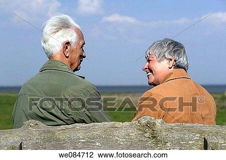 Elderly couple sitting on a bench, seen from backside and smiling at each other, Island of Amrum, North Frisian Islands, Schleswig-Holstein, Northern Germany View Large Photo Image Stock Image - Elderly couple sitting on a bench, seen from backside and smiling at each other, Island of Amrum, North Frisian Islands, Schleswig-Holstein, Northern Germany. Fotosearch