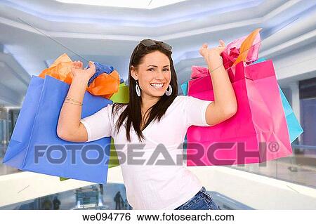 Excited Caucasian woman holding shopping bags and smiling in a shopping mall View Large Photo Image Stock Photograph - Excited Caucasian woman holding shopping bags and smiling in a shopping mall. Fotosearch