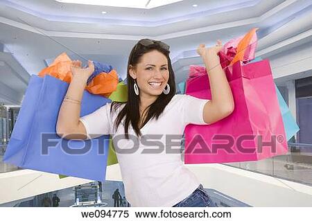 Excited Caucasian woman holding shopping bags and smiling in a shopping mall View Large Photo Image Stock Photography - Excited Caucasian woman holding shopping bags and smiling in a shopping mall. Fotosearch
