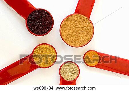 Picture - Five red measuring spoons, from a tablespoon to a quarter teaspoon, filled with Indian spices arranged in a geometric pattern on a white background Spices include chili powder, ground cinnamon, turmeric, coriander, and curry powder. Fotosearch