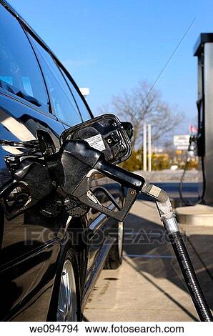 Picture - Gas pump nozzle inserted into a black car while refueling at a gas station in Canadian winter. Fotosearch
