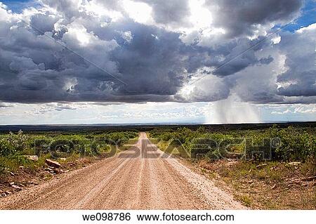 Isolated thundershower falling from looming cumulus cloud formations while sun shines on dirt road leading into the distance View Large Photo Image Stock Photograph - Isolated thundershower falling from looming cumulus cloud formations while sun shines on dirt road leading into the distance. Fotosearch