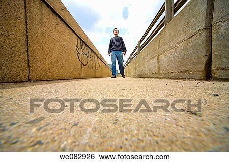 Low-angle view of a man standing on a pedestrian bridge View Large Photo Image Stock Photograph - Low-angle view of a man standing on a pedestrian bridge. Fotosearch