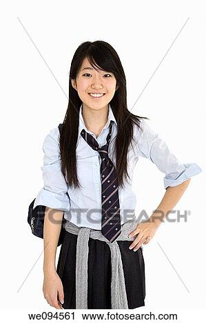 Stock Image - Portrait of a female Asian teenager dressed in the traditional Japanese schoolgirl clothing Uniforms are worn by most of the female school children in Japan She is standing on a white background and smiling. Fotosearch