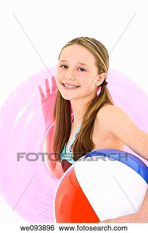 Stock Photograph - Preteen caucasian girl standing on a white background in a swimsuit holding beach toys and smiling. Fotosearch