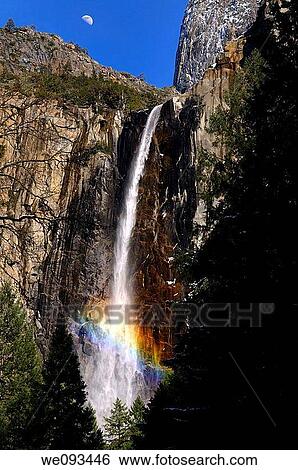 Stock Photograph - Rainbow in the mist of Bridalveil Fall at Cathedral Rocks with half moon. Fotosearch