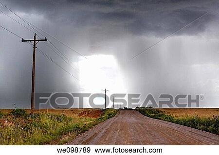 Rural thunderstorm scene showing dirt road leading to a bright light opening up between looming cumulus thunder clouds releasing rain View Large Photo Image Stock Photo - Rural thunderstorm scene showing dirt road leading to a bright light opening up between looming cumulus thunder clouds releasing rain. Fotosearch