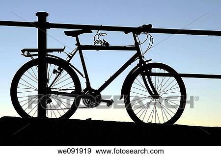 Silhouette of bicycle chained up on seaside jetty at dusk View Large Photo Image Stock Photo - Silhouette of bicycle chained up on seaside jetty at dusk. Fotosearch