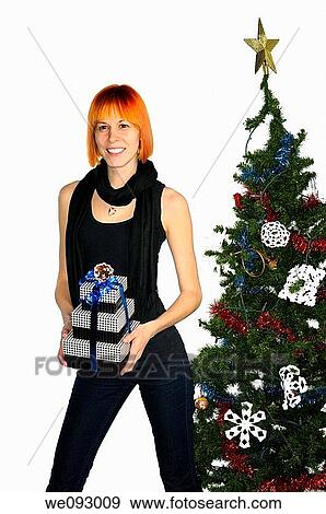 Smiling tall woman with red hair holding Christmas presents by a decorated tree View Large Photo Image Stock Photo - Smiling tall woman with red hair holding Christmas presents by a decorated tree. Fotosearch