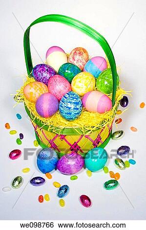 Straw Easter basket filled with eggs of different colors and patterns, with more eggs, jelly beans, and foil covered chocolates spilling over View Large Photo Image Stock Photograph - Straw Easter basket filled with eggs of different colors and patterns, with more eggs, jelly beans, and foil covered chocolates spilling over. Fotosearch