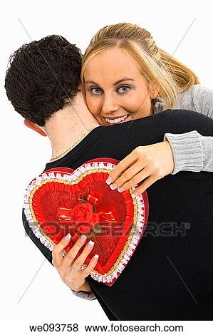 Studio photograph of young Caucasian couple posing with their arms around each other and holding a Valentine heart on a white background View Large Photo Image Stock Photo - Studio photograph of young Caucasian couple posing with their arms around each other and holding a Valentine heart on a white background. Fotosearch