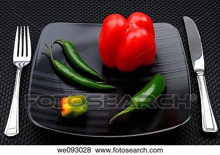 Stock Photo - Table setting with cutlery and black plate with sweet belll and hot chili peppers. Fotosearch