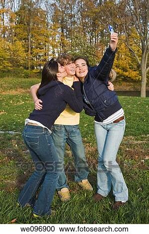 Three caucasian teens one male and two females horsing around in a park using a cell phone to take their pictures View Large Photo Image Stock Image - Three caucasian teens one male and two females horsing around in a park using a cell phone to take their pictures. Fotosearch