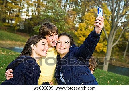 Three caucasian teens one male and two females horsing around in a park using a cell phone to take their pictures View Large Photo Image Stock Photo - Three caucasian teens one male and two females horsing around in a park using a cell phone to take their pictures. Fotosearch
