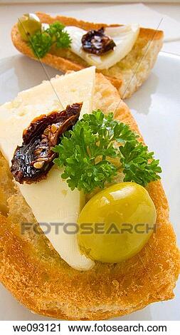 Stock Image - Toasted bread with cheese, dried tomato and olives. Fotosearch