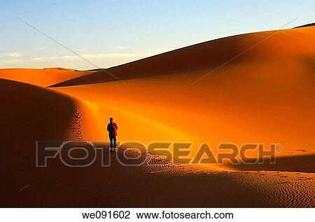 Tourist walking at sunset in the sand dunes of the Erg Muzuruq, Sahara desert, Libya View Large Photo Image Stock Image - Tourist walking at sunset in the sand dunes of the Erg Muzuruq, Sahara desert, Libya. Fotosearch