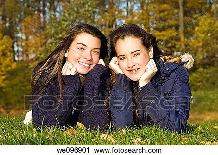 Stock Image - Two caucasian female teens laying on grass posing for a picture. Fotosearch