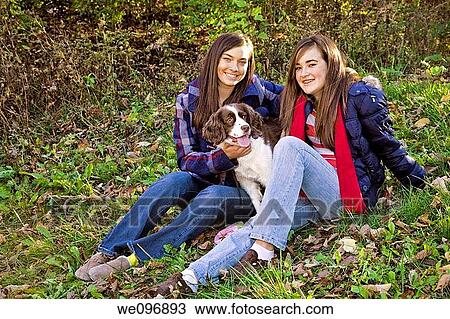 Stock Image - Two caucasian female teens sitting in the park with their dog. Fotosearch