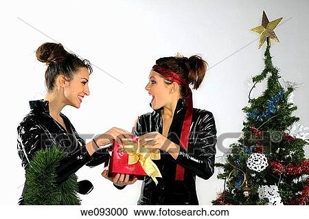Two young women in black plastic catsuits opening a present by a Christmas tree on white background View Large Photo Image Stock Image - Two young women in black plastic catsuits opening a present by a Christmas tree on white background. Fotosearch