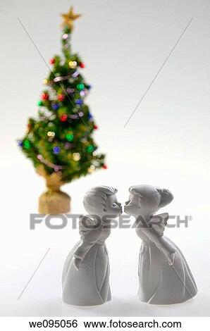 Stock Photograph - White porcelain boy and girl angels kissing in front of a decorated Christmas Tree. Fotosearch