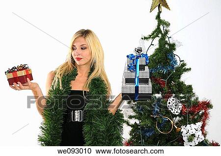 Woman standing by a Christmas tree contemplating presents in her hands View Large Photo Image Stock Image - Woman standing by a Christmas tree contemplating presents in her hands. Fotosearch