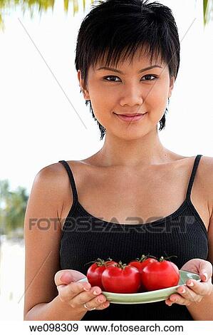 Young asian woman holding plate of tomatoes View Large Photo Image Stock Photo - Young asian woman holding plate of tomatoes. Fotosearch