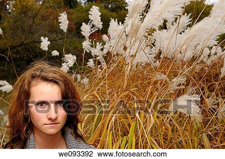 Stock Image - Young girl standing by a river in the Fall with tall wild white plumed Pampas Grass. Fotosearch