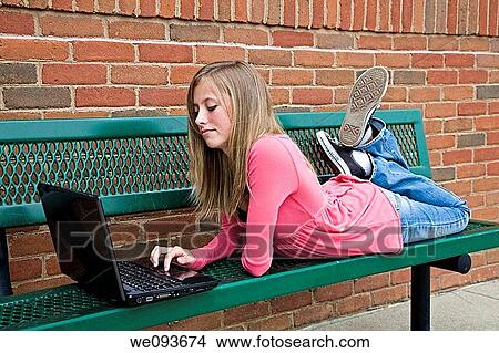 Young teenage girl laying down and working on a laptop computer outside a school View Large Photo Image Picture - Young teenage girl laying down and working on a laptop computer outside a school. Fotosearch