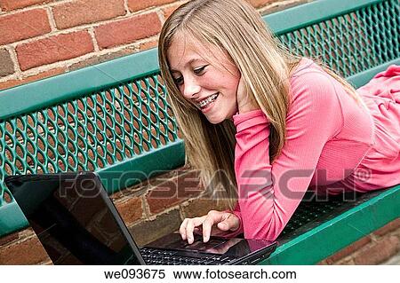 Stock Photography - Young teenage girl laying down and working on a laptop computer outside a school. Fotosearch