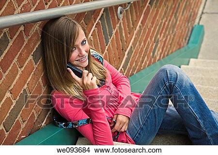 Picture - Young teenage girl talking on cell phone outside of a school building. Fotosearch