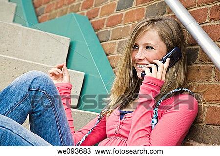 Stock Image - Young teenage girl talking on cell phone outside of a school building. Fotosearch