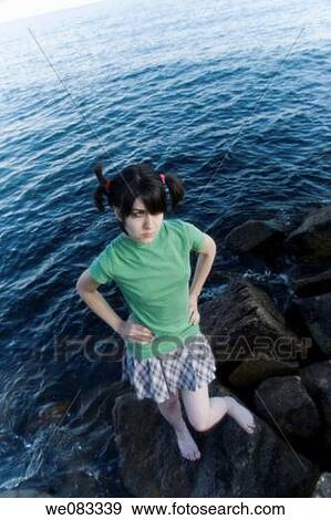 Stock Photo - Young woman, her hair in pigtails, standing on a rock in the ocean.. Fotosearch
