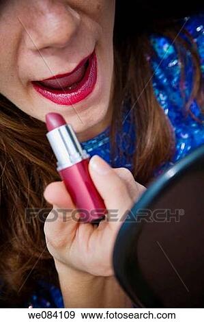 Stock Photo - Young woman, holding a mirror, applying lipstick. Fotosearch