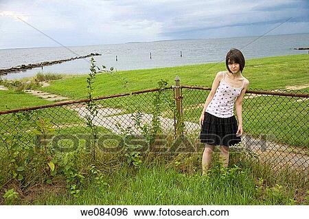 Young woman standing in front of a chain-link fence and the ocean. View Large Photo Image Stock Photograph - Young woman standing in front of a chain-link fence and the ocean.. Fotosearch
