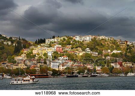 Stock Photo - Sun on homes on a hillside of Arnavutkoy Besiktas Istanbul with storm clouds on the Bosphorus Strait. Fotosearch