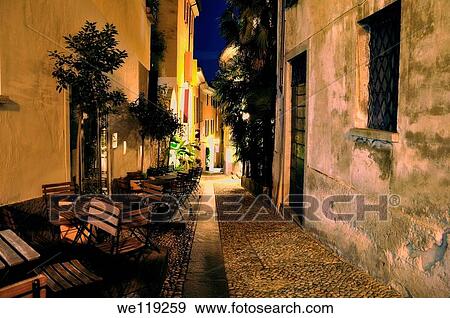 Old alley illuminated at night with chairs and tables View Large Photo Image Stock Photo - Old alley illuminated at night with chairs and tables. Fotosearch