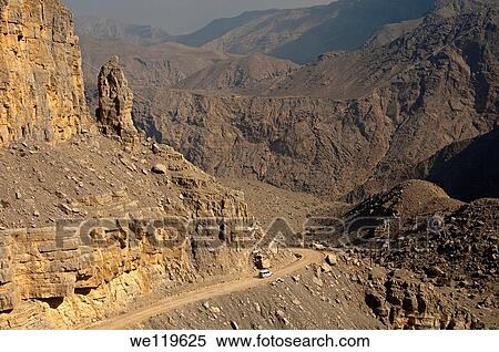 Stock Photography - White off-road vehicle on a rough road amidst the rugged mountains on the way to Mount Jebel Harim, Musandam peninsula, Sultanate of Oman. Fotosearch