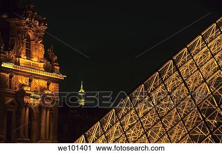 Stock Image - The Louvre Pyramid illuminated at night, with the tip of the Eiffel Tower in the distance, Paris, France.. Fotosearch