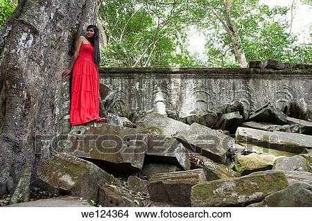 Beautiful Cambodian woman wearing a red dress posing beside a tree in Ta Phrom temple in Angkor Cambodia. View Large Photo Image Picture - Beautiful Cambodian woman wearing a red dress posing beside a tree in Ta Phrom temple in Angkor Cambodia.. Fotosearch